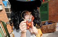 A child wearing a wig, beard and hat as a disguise looks through a magnifying glass and points to the camera